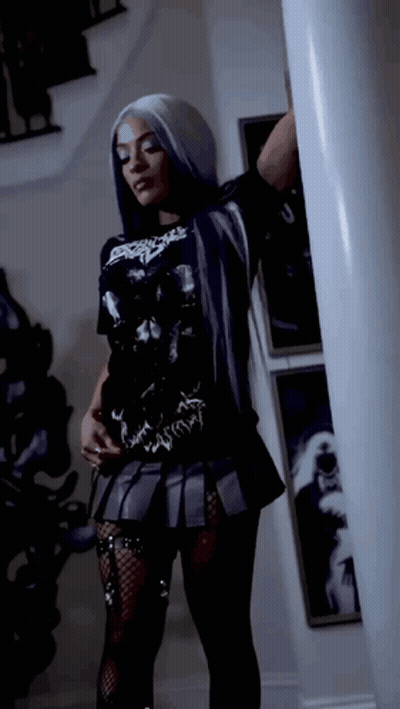 Woman In Black T-Shirt And Skirt Standing Next To Pillar GIF