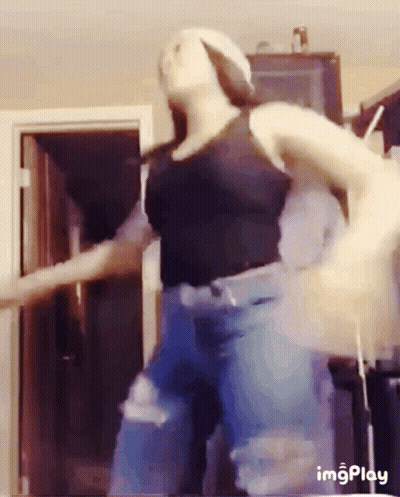 Woman In Black Tank Top And Blue Jeans Dancing In Front Of Door GIF