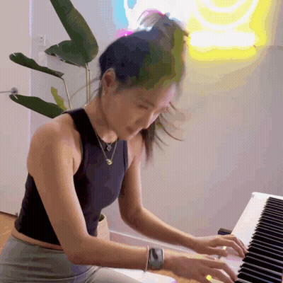 Woman In Black Tank Top Playing Piano In Front Of SpongeBob Neon Sign GIF