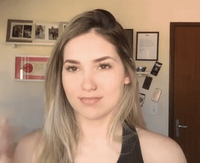 Woman In Black Tank Top Standing In Front Of Wall With Pictures And Sign Saying A GIF
