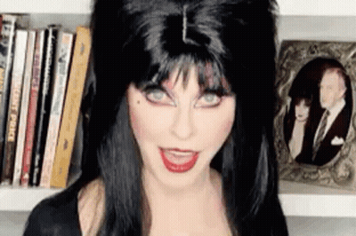 Woman In Black Wig In Front Of Bookshelf GIF