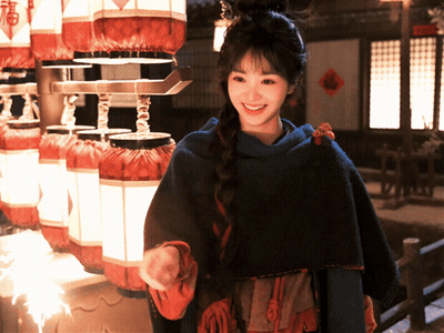 Woman In Blue Cape Smiling In Front Of Lanterns GIF