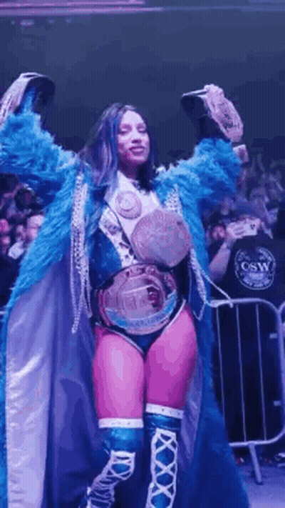 Woman In Blue Coat Holding Two Championship Belts GIF