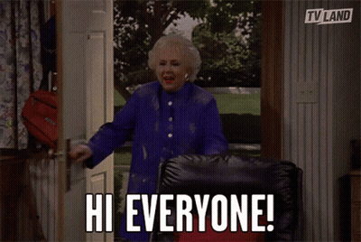 Woman In Blue Coat Standing In Doorway Says Hi Everyone GIF