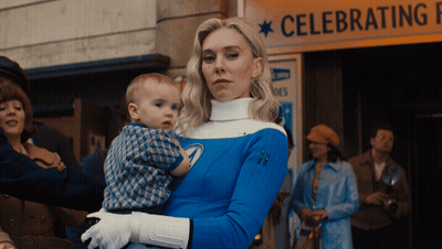 Woman In Blue Costume Holding Baby In Front Of Celebrating Sign GIF