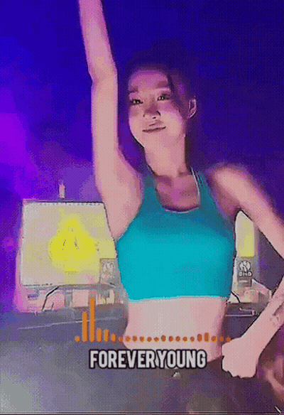 Woman In Blue Crop Top Dancing In Front Of Forever Young Sign GIF