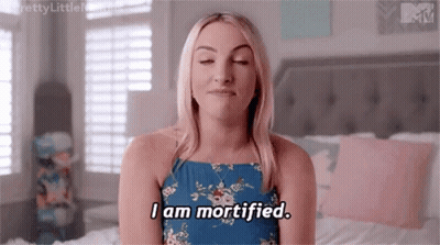 Woman In Blue Dress Sitting On Bed Eyes Closed Saying I Am Mortified GIF
