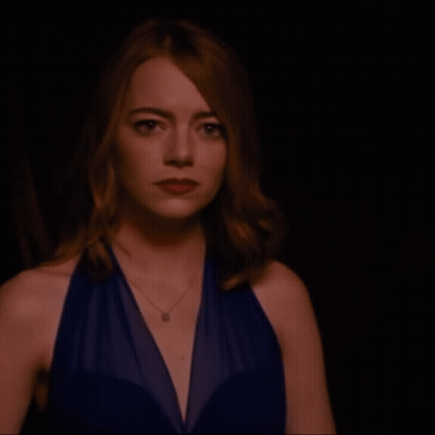 Woman In Blue Dress With Necklace Looking At Camera GIF