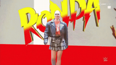 Woman In Blue Jacket And Plaid Skirt In Front Of Ronda Sign GIF