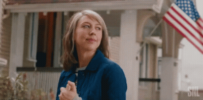 Woman In Blue Jacket In Front Of House With American Flag GIF