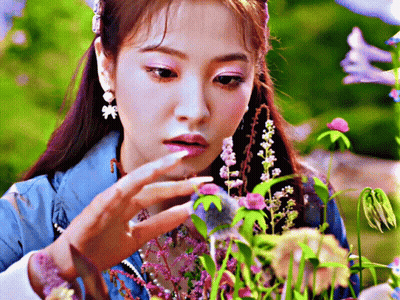 Woman in Blue Jacket Looking at Purple Flowers