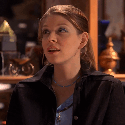 Woman In Blue Necklace And Black Jacket Looks To Side GIF
