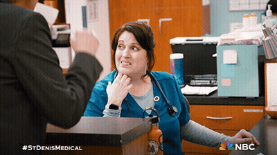 Woman In Blue Scrub Talking To Man In Black Suit With NBC Logo GIF