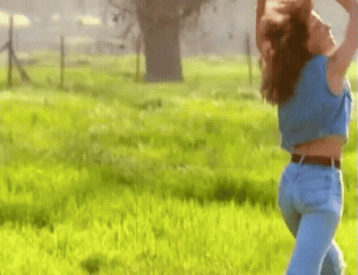 Woman In Blue Shirt And Jeans Standing In Grass Field GIF