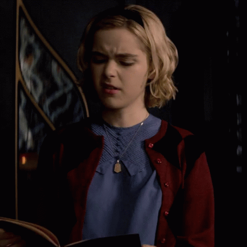Woman In Blue Shirt And Red Cardigan Looking At Book GIF