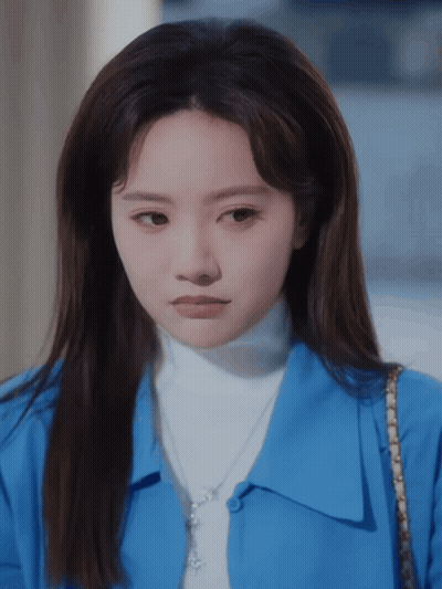 Woman In Blue Shirt And White Turtleneck Looking At Camera GIF