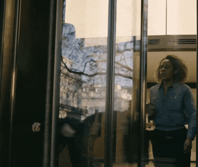 Woman In Blue Shirt In Glass Doorway GIF