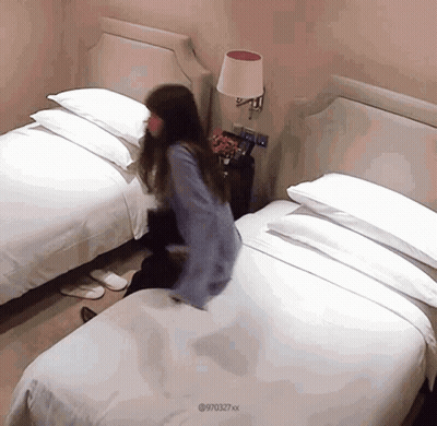 Woman In Blue Shirt Jumping On Hotel Bed GIF
