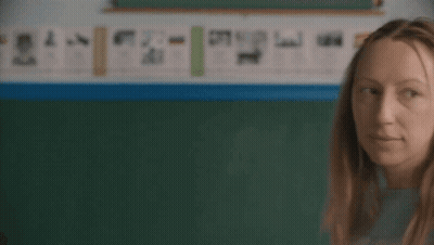 Woman In Blue Shirt Scratching Head In Front Of Blackboard GIF