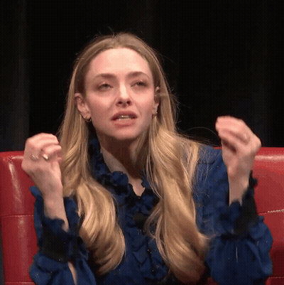 Woman In Blue Shirt Sitting On Red Couch With Hands Up GIF