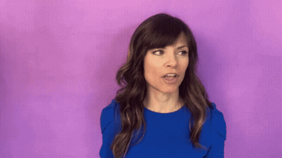 Woman In Blue Shirt Surprised In Front Of Purple Wall GIF