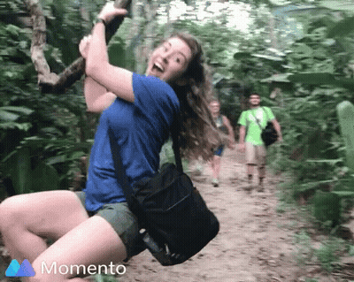 Woman In Blue Shirt Swinging On Rope In Woods With Momento Logo GIF