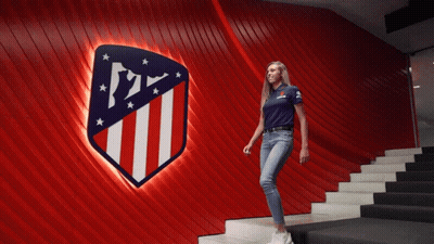 Woman In Blue Shirt Walking Down Stairs In Front Of Atlético Madrid Sign GIF