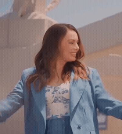 Woman In Blue Suit And Floral Top Smiling With Arms Outstretched GIF