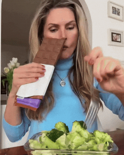 Woman In Blue Sweater Eating Broccoli And Milka Chocolate GIF