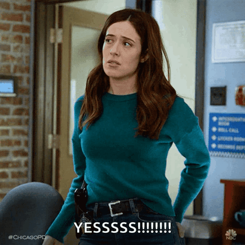 Woman In Blue Sweater Says Yesssss In Front Of Brick Wall GIF
