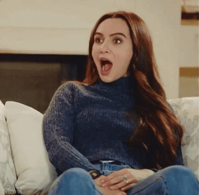 Woman In Blue Sweater With Mouth Open On Couch GIF