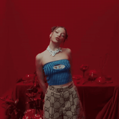Woman In Blue Top And Gucci Skirt In Front Of Red Wall GIF