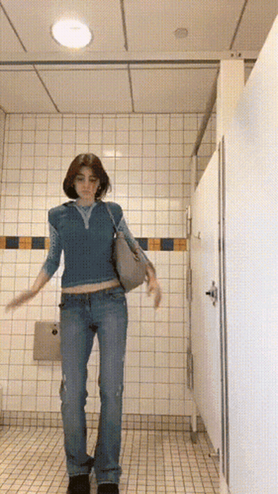 Woman In Blue Top And Jeans In Public Restroom GIF