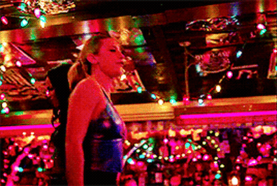 Woman In Blue Top Standing Under Christmas Lights GIF