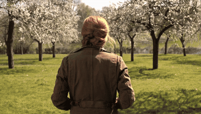 Woman In Brown Jacket Walking Through Blooming Park GIF