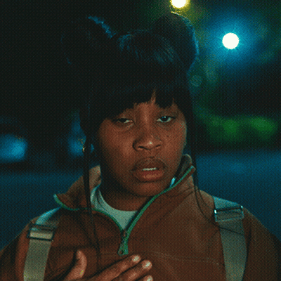 Woman In Brown Jacket With Green Zipper Hand To Chest GIF