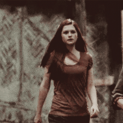 Woman In Brown Shirt In Front Of Stone Wall GIF