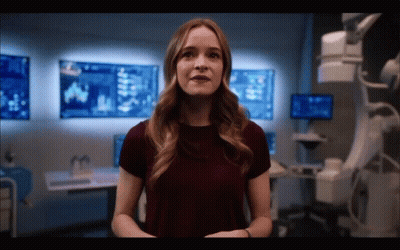 Woman In Burgundy Shirt Standing In Front Of Wall With Monitors GIF