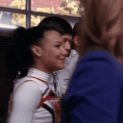 Woman In Cheerleading Uniform Smiling At Man In Blue Shirt GIF