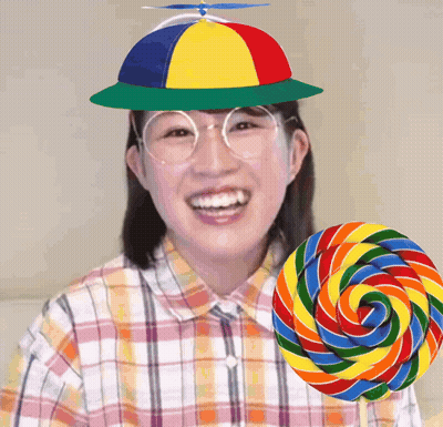 Woman In Colorful Hat And Glasses Smiling Next To Lollipop GIF