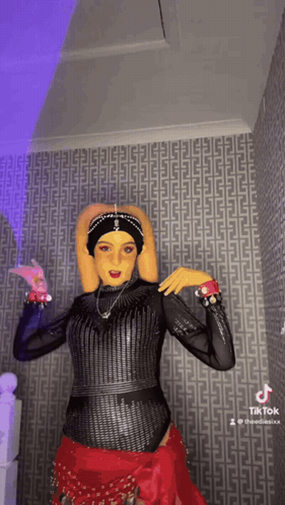 Woman In Costume Dancing In Front Of Patterned Wall GIF