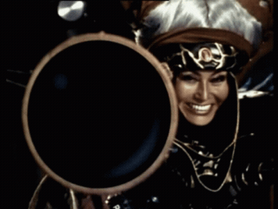 Woman In Costume Holding Large Object And Smiling GIF
