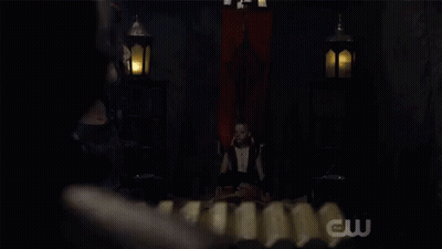 Woman In Costume In Dark Room With CW Logo GIF
