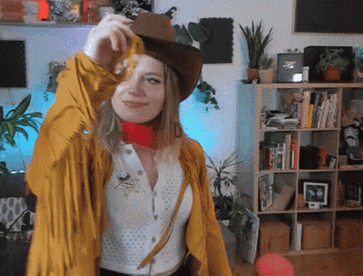 Woman In Cowboy Hat And Yellow Jacket In Front Of Bookshelf GIF