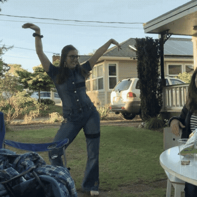 Woman in Denim Jumpsuit with Arms Up Outside House