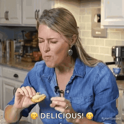 Woman In Denim Shirt Eating Cookie Saying Delicious GIF