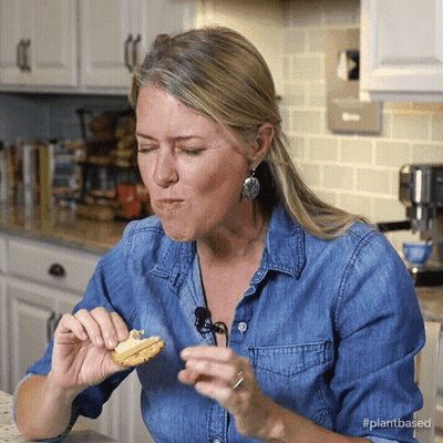 Woman In Denim Shirt Eating Food With Hashtag PlantBased GIF