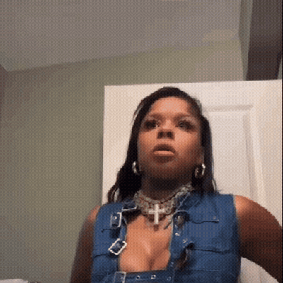 Woman In Denim Vest And Cross Necklace Sitting By Door GIF