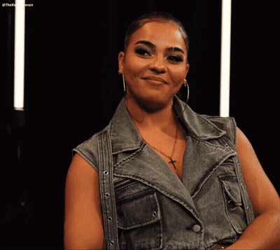 Woman In Denim Vest And Hoop Earrings Smiling GIF
