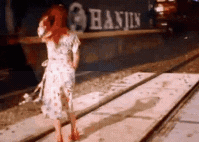 Woman In Dress Standing On Train Track In Front Of Train GIF